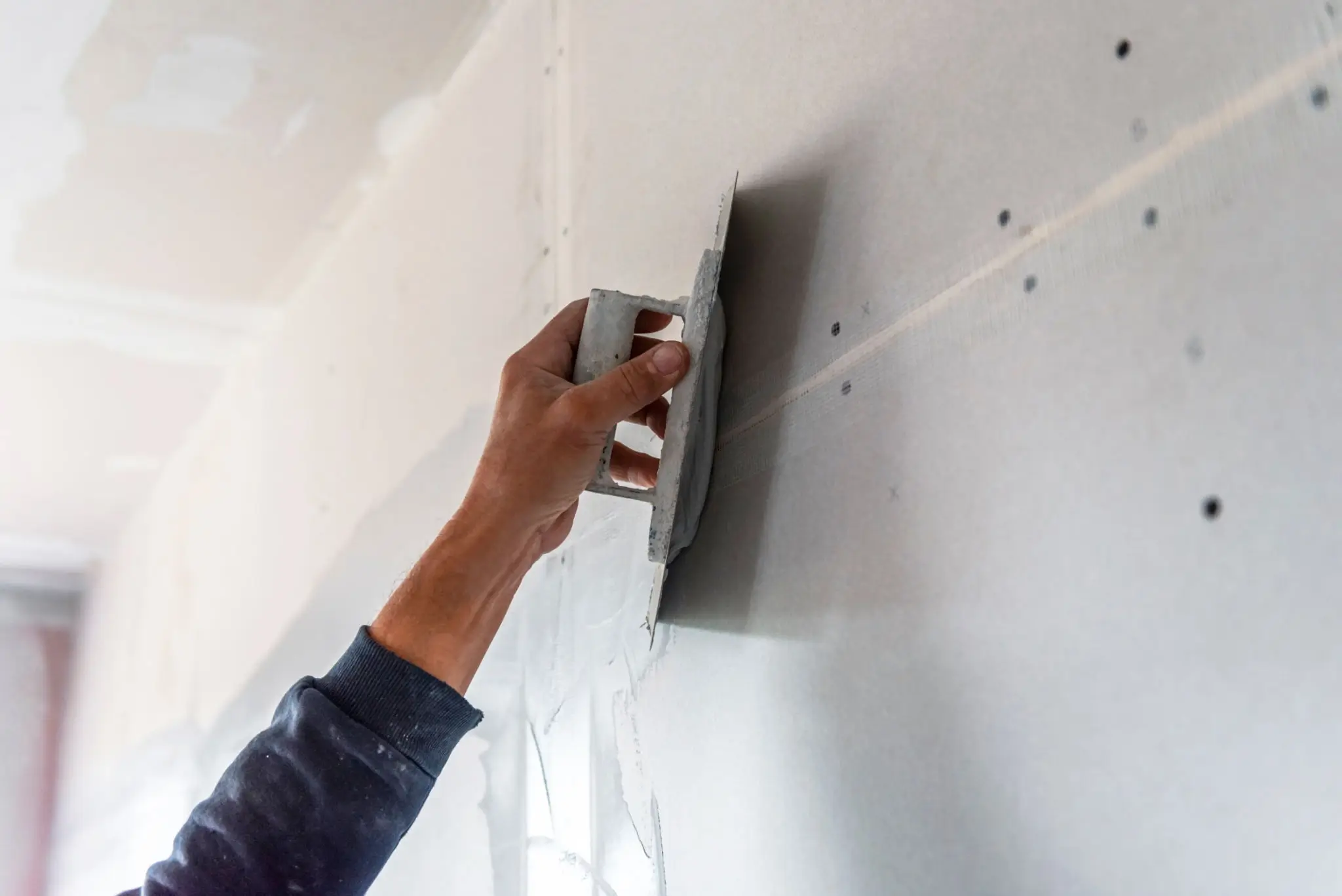 Person smoothing plaster on a wall with a trowel.